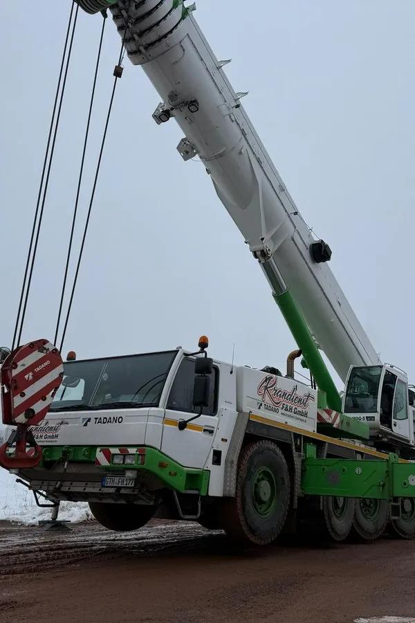 Weiß-grüner Autokran mit ausgefahrenem Ausleger auf einer winterlichen Baustelle