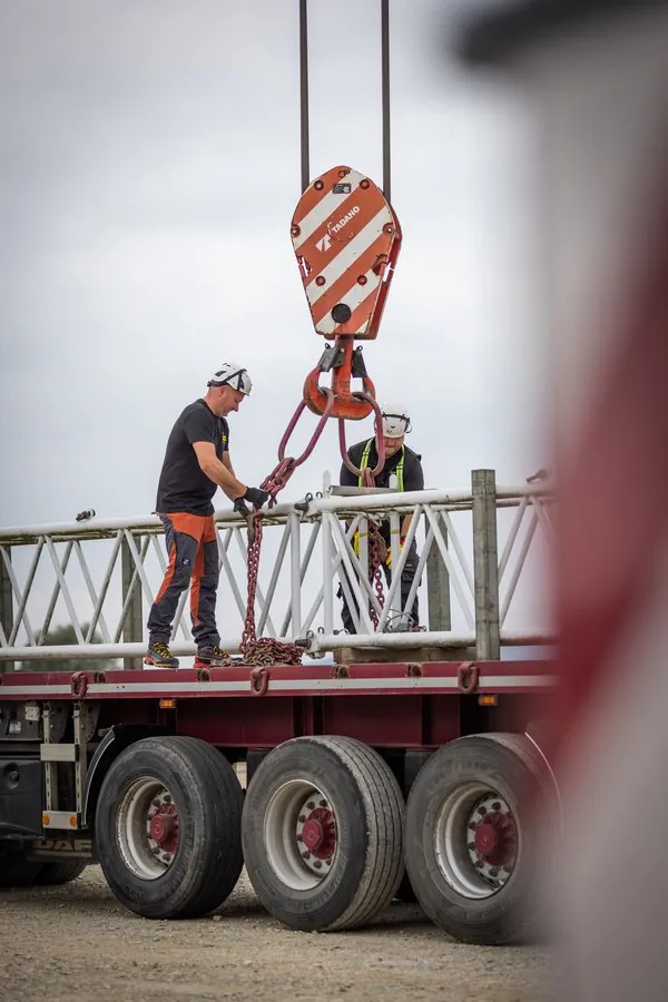 Monteure schlagen eine Traverse auf einem Tieflader am Kranhaken an